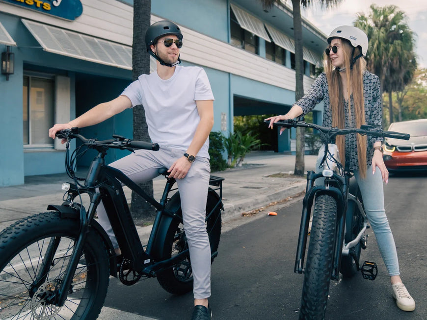 Two people on electric bikes in an urban setting with a building and car in the background. Valowave Ranger 2.0 Fat Tire All-Terrain Electric Bike