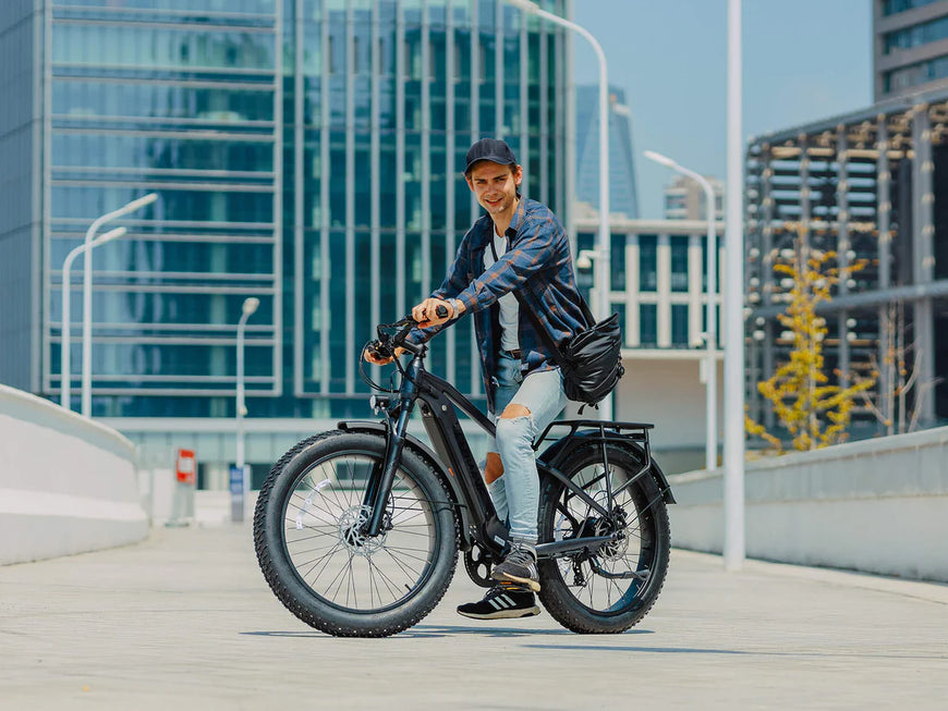 Man riding an electric bike in an urban setting with modern buildings in the background. Valowave Ranger 3.0 Fat Tire All-Terrain Electric Bike