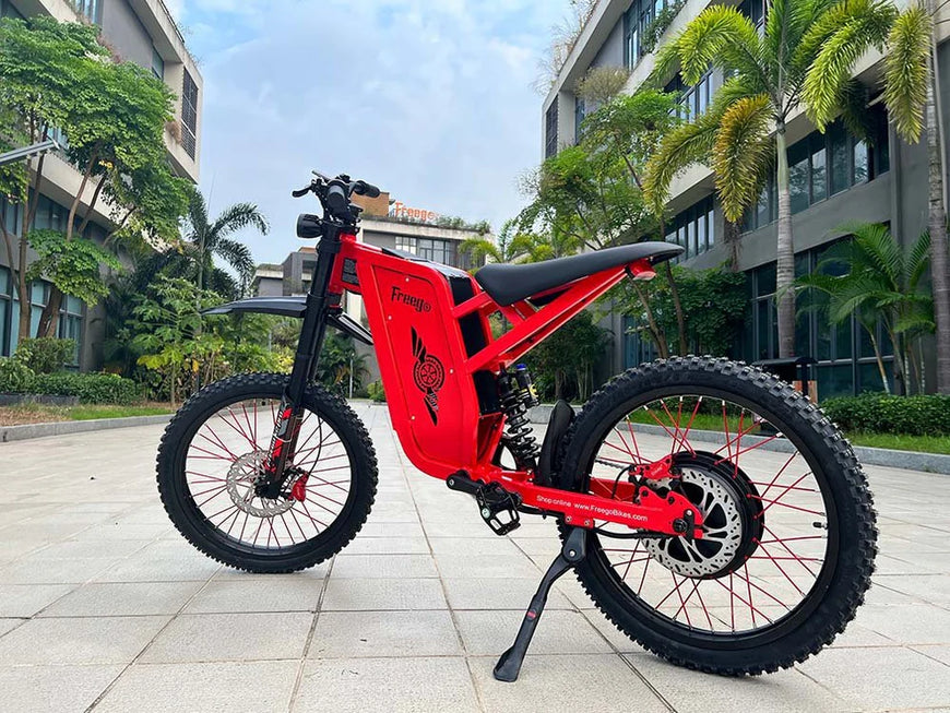Red electric bike on a paved area with buildings and trees in the background. Freego X2 Pro All-Terrain Dirt eBike