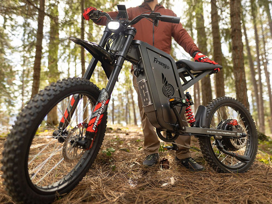 Person holding a Freyco electric bike in a forest setting. Freego X2 Pro All-Terrain Dirt eBike
