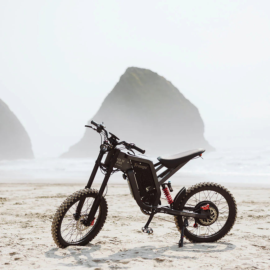Black electric bike on a sandy surface with large white structures in the background. Freego X2 Pro All-Terrain Dirt eBike
