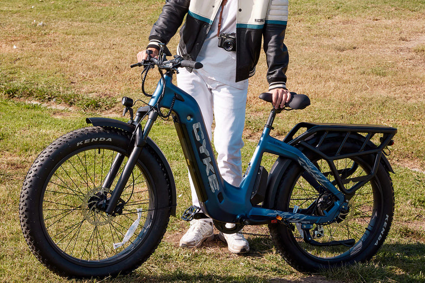 Person holding a blue electric bike with visible branding outdoors on grass. CYKE Lynx Commuter EBike