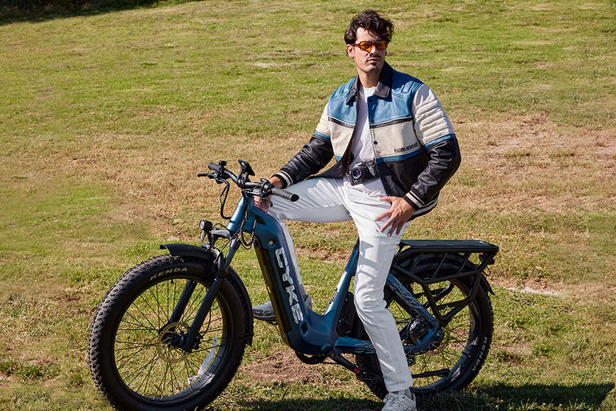 Person sitting on a blue electric bike in a grassy field. CYKE Lynx Commuter EBike