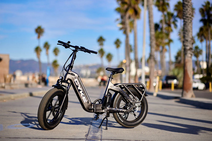 Electric bike on a sidewalk with palm trees and a clear sky in the background. CYKE Grizzly Foldable EBike