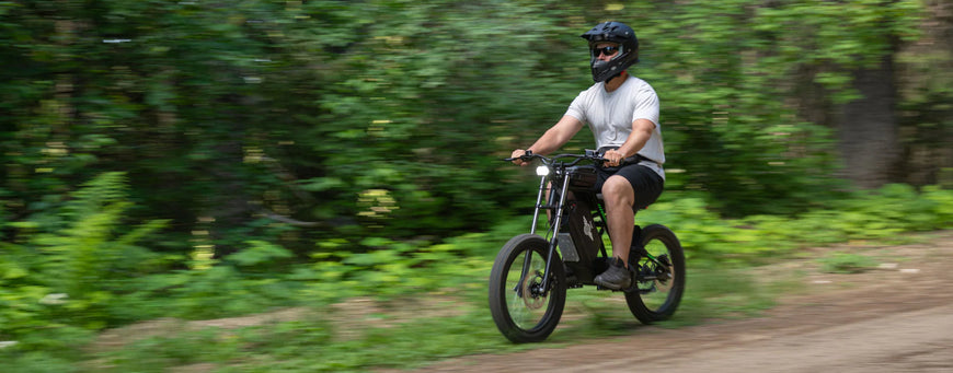 Person riding a small bike on a trail with greenery in the background. Freego Nova 3 Mid-Drive All-Terrain Dirt eBike