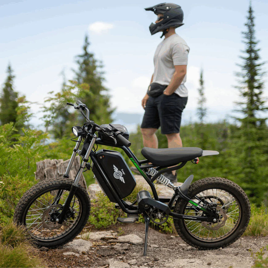 Person standing next to an electric bike in a forested area. Freego Nova 3 Mid-Drive All-Terrain Dirt eBike