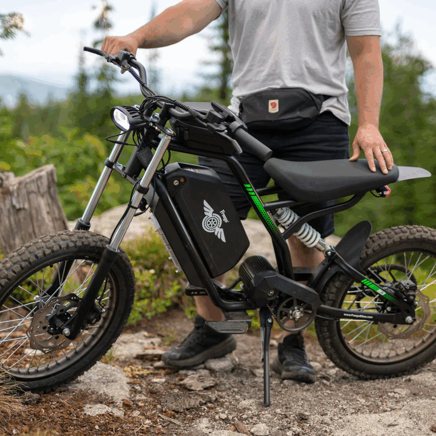 Person standing next to an electric bike on a trail with greenery in the background Freego Nova 3 Mid-Drive All-Terrain Dirt eBike