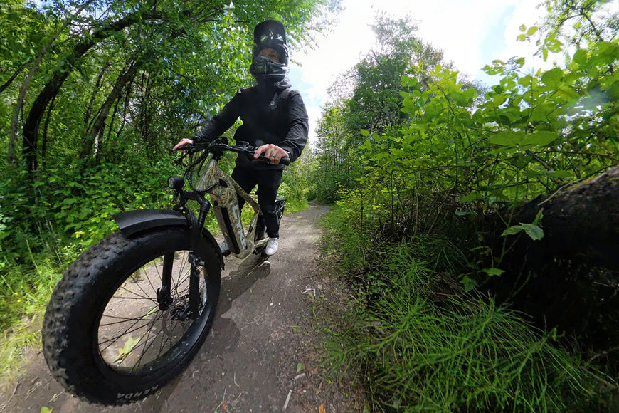 Person riding a fat-tire bike on a trail surrounded by greenery. CYKE Cheetah Hunting EBike
