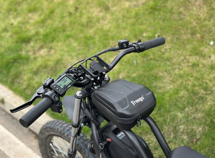 Close-up of a black electric bike handlebar with a visible brand logo against a grassy background. Freego Nova 3 Mid-Drive All-Terrain Dirt eBike
