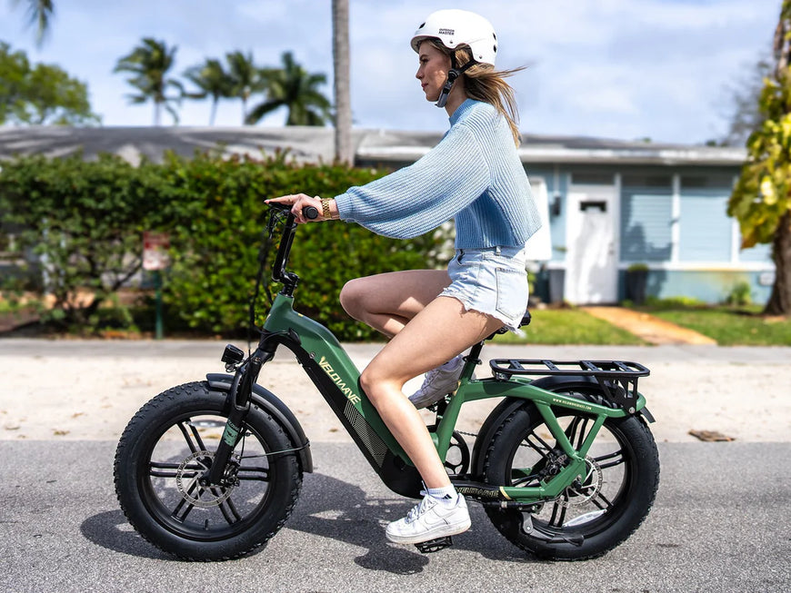 Woman riding a green electric bike on a residential street. Valowave Pony Compact Step-Thru Electric Bike