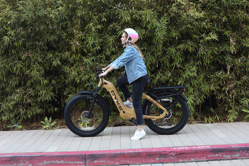 Person riding a electric bike on a sidewalk with greenery in the background. CYKE Lynx Commuter EBike