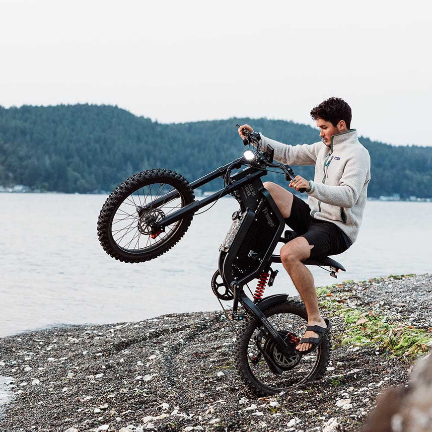 Person sitting on a unique bicycle by a lake with mountains in the background. Freego X2 Pro All-Terrain Dirt eBike